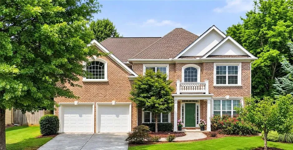 Brick facade residence featuring a two-car garage, a covered front entry with columns, and a second-story balcony