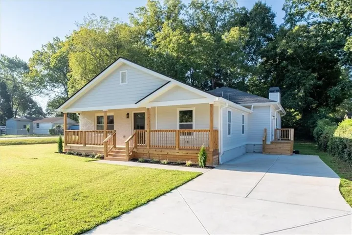 Light-colored siding exterior with a dark-shingled roof and a prominent front porch with natural wood railings