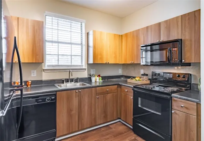 Kitchen featuring dark wood-type flooring, black appliances, sink, and backsplash