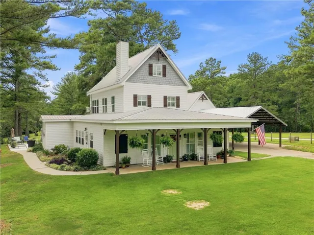 Charming farmhouse-style home featuring a classic two-story design with board-and-batten siding, a covered front porch with supporting columns, and a wraparound covered structure extending across the front facade