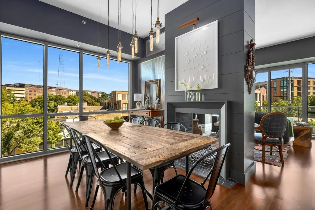 Dramatic tall ceilings and floor-to-ceiling windows create an airy atmosphere, while the living area features a striking, decorative fireplace with shiplap surround and seamless flow into the chef's kitchen.