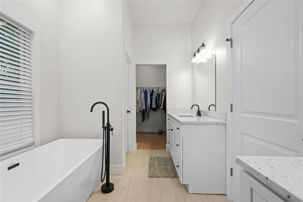 Bathroom featuring vanity, a freestanding bath, a spacious closet, and light wood-style floors