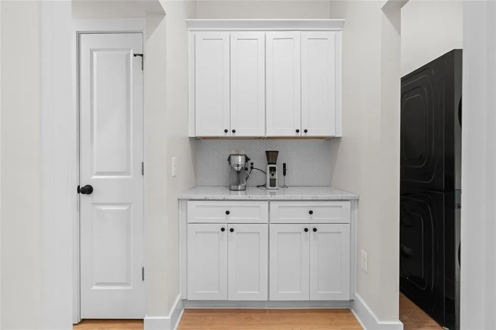Bar featuring white cabinetry, light stone counters, light wood-style floors, and stacked washer / dryer