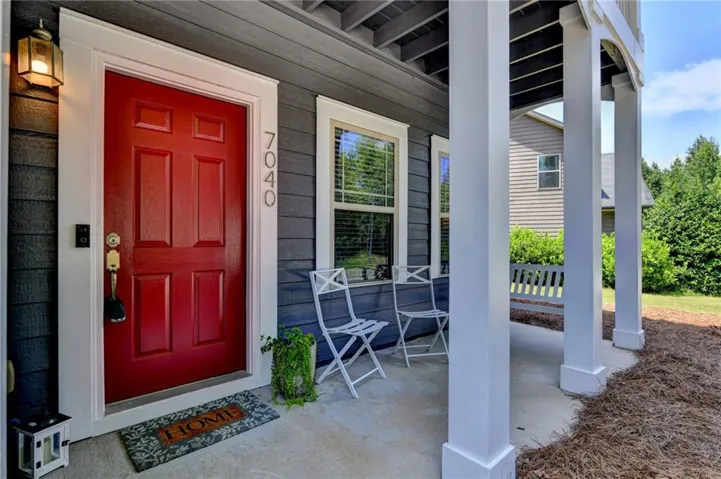 Red paneled entry door with white trim, dark gray siding, and a covered porch supported by white columns