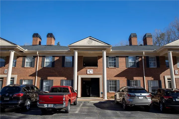 Brick facade building with a dark shingle roof, featuring multiple prominent brick chimneys and white column accents