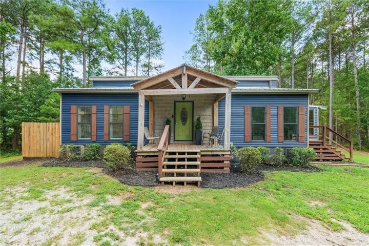 Blue horizontal siding exterior with wood shutters, a covered front porch featuring exposed wood beams, and a bright green front door
