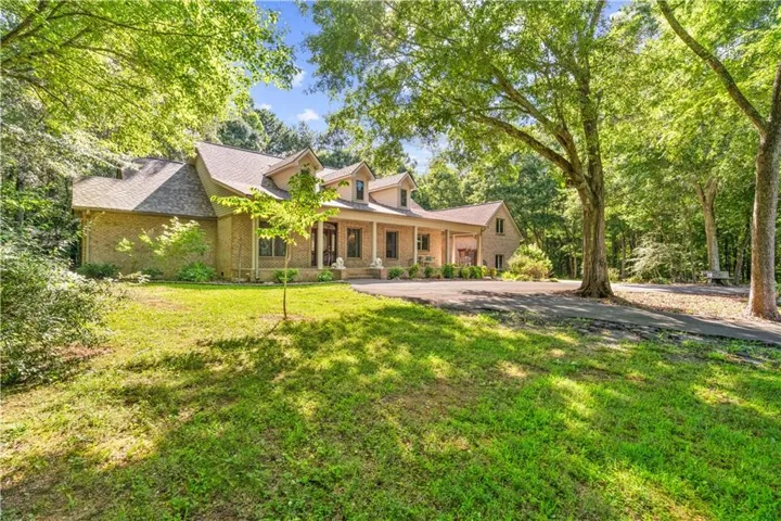 Expansive tree-lined property featuring a brick exterior, gabled rooflines, and a covered front porch with columns