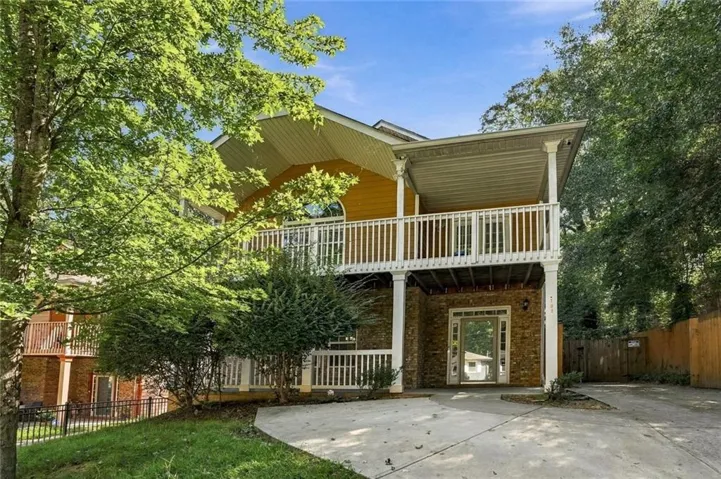 Split-level exterior with a stone-clad lower level, yellow siding, and a covered upper balcony