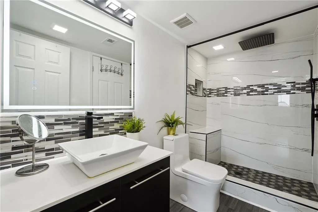 Bathroom featuring backsplash, toilet, vanity, and a tile shower