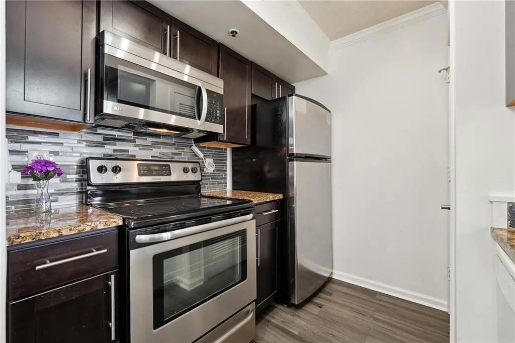 Kitchen with light stone countertops, dark wood-type flooring, backsplash, stainless steel appliances, and dark brown cabinetry