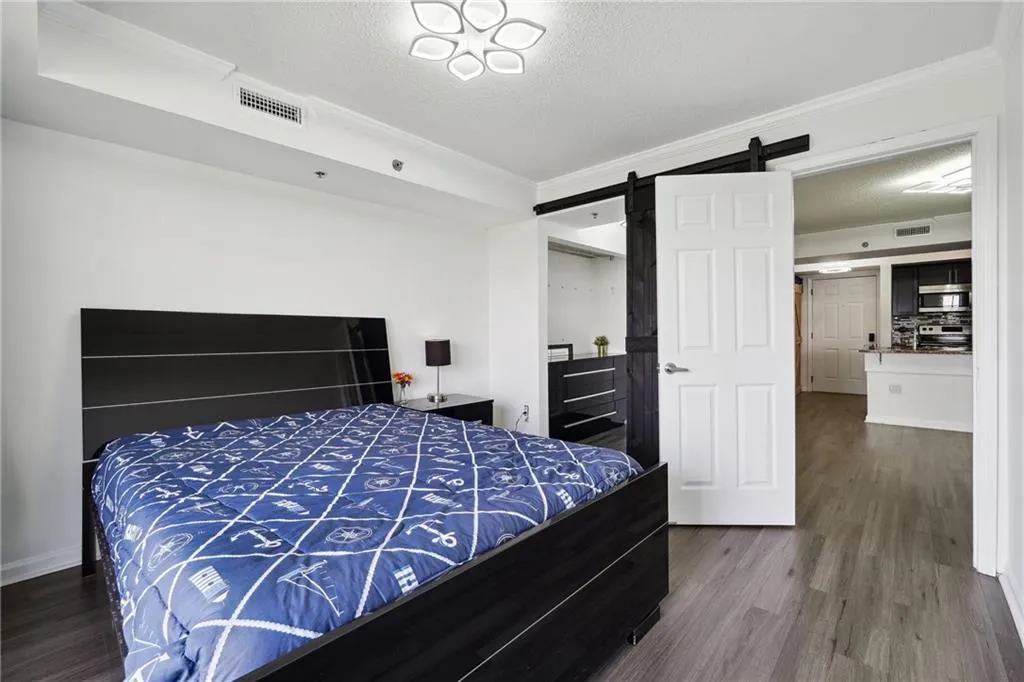 Bedroom featuring hardwood / wood-style flooring, ornamental molding, and a barn door