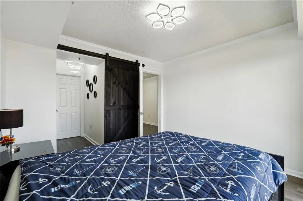 Bedroom featuring hardwood / wood-style floors, ornamental molding, a barn door, and a textured ceiling