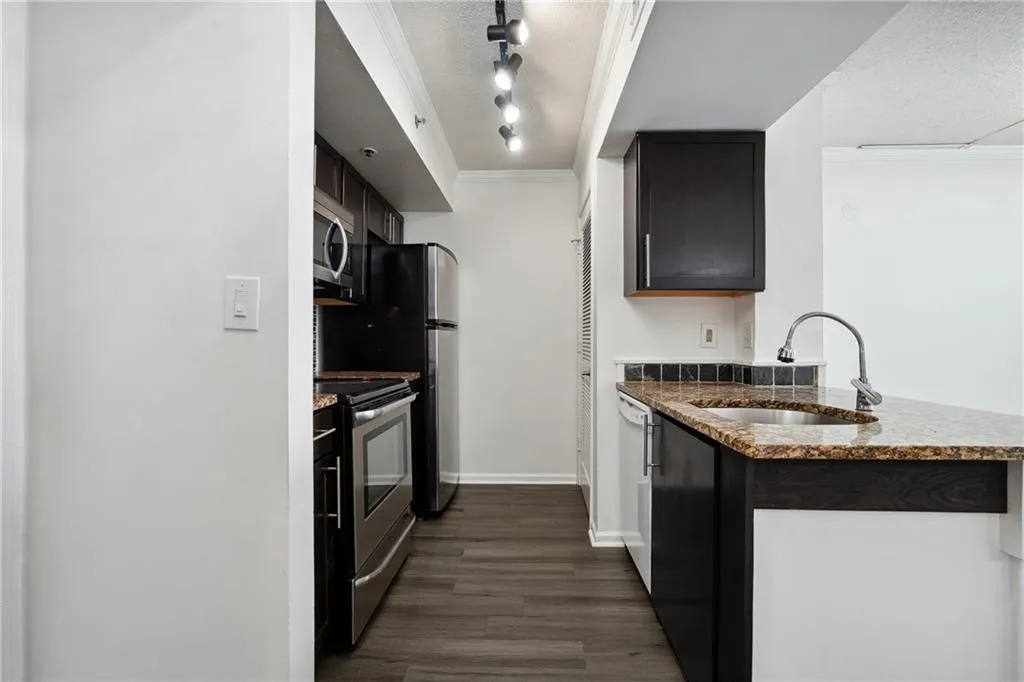 Kitchen with appliances with stainless steel finishes, track lighting, a textured ceiling, sink, and dark hardwood / wood-style flooring