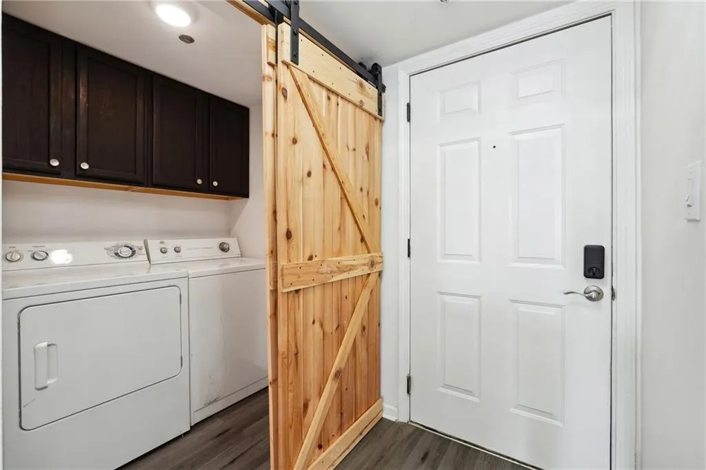 Clothes washing area with washer and clothes dryer, a barn door, dark hardwood / wood-style flooring, and cabinets