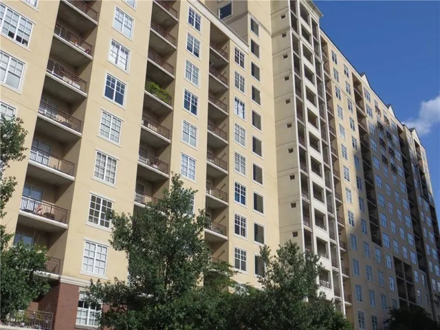 Multi-story building featuring numerous private balconies with metal railings, a light-colored stucco exterior, and multi-pane windows