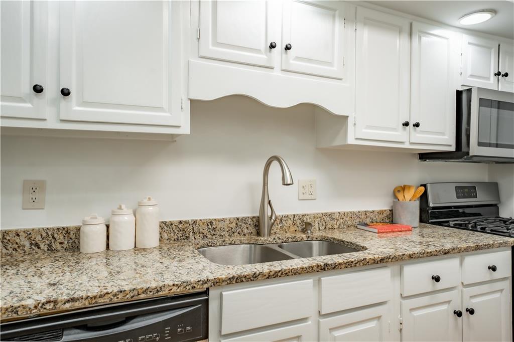 Kitchen with white cabinetry, sink, light stone countertops, and stainless steel appliances