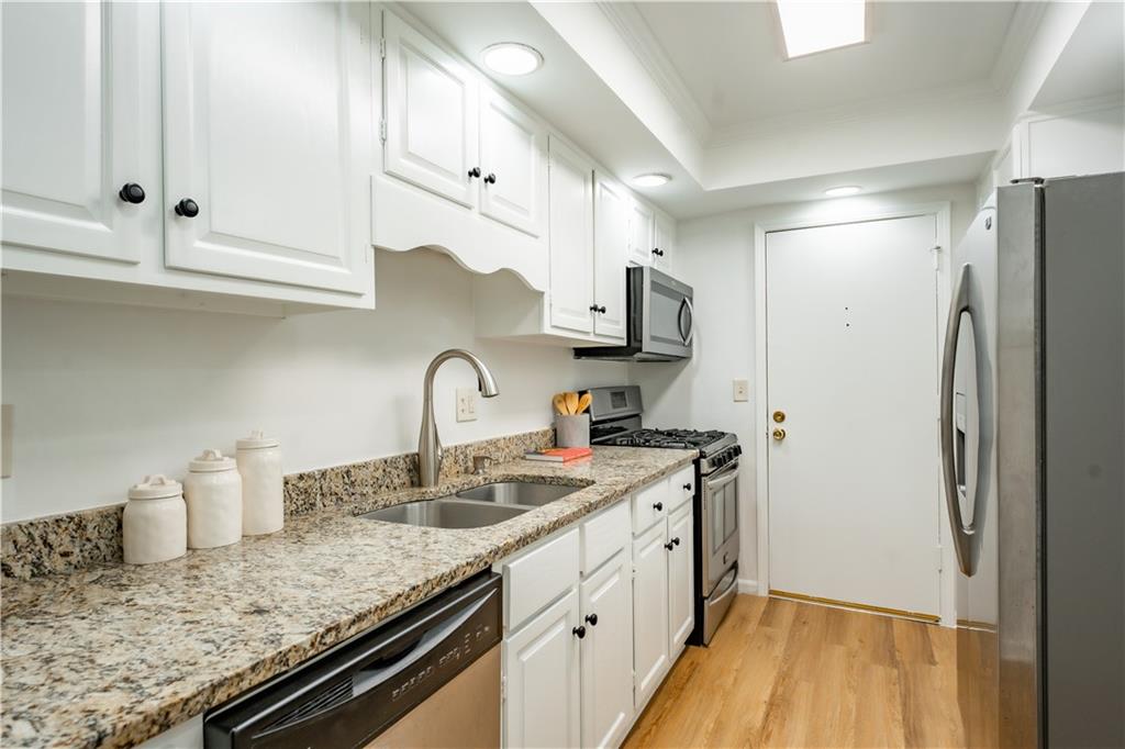 Kitchen with light stone countertops, appliances with stainless steel finishes, light hardwood / wood-style flooring, and white cabinetry