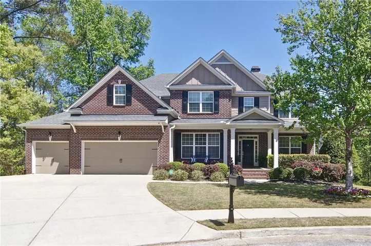 Brick Colonial two-story home featuring a welcoming front facade with peaked gable rooflines, multiple windows with dark shutters, and a covered front porch entry