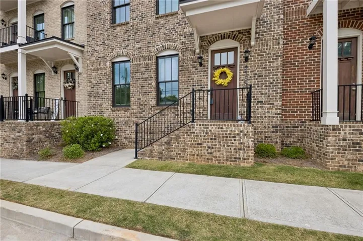 Brick facade townhome featuring arched windows, dark wood-finish entry doors, black iron railings, and a covered front porch