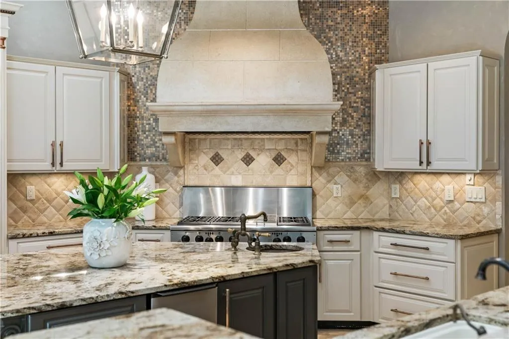 Kitchen with light stone countertops, decorative backsplash, a chandelier, and white cabinetry