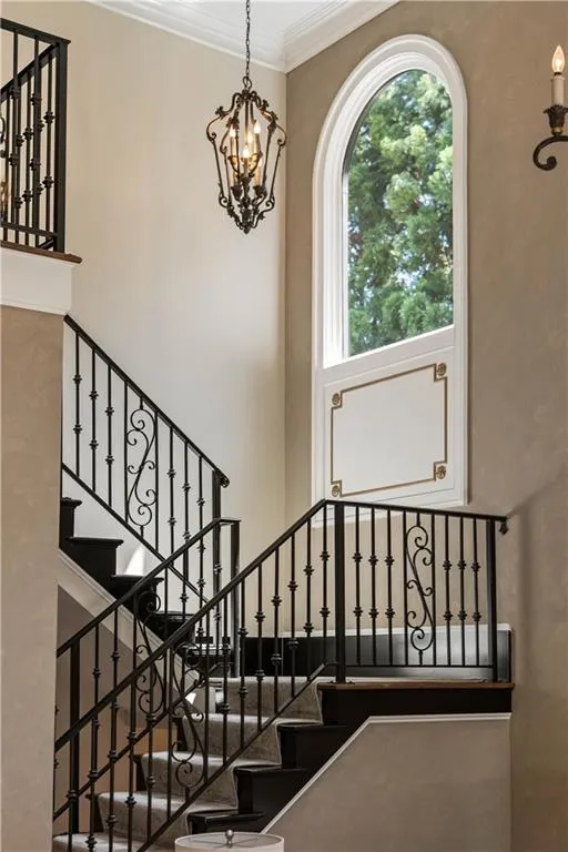 Stairway featuring ornamental molding, an inviting chandelier, and a high ceiling