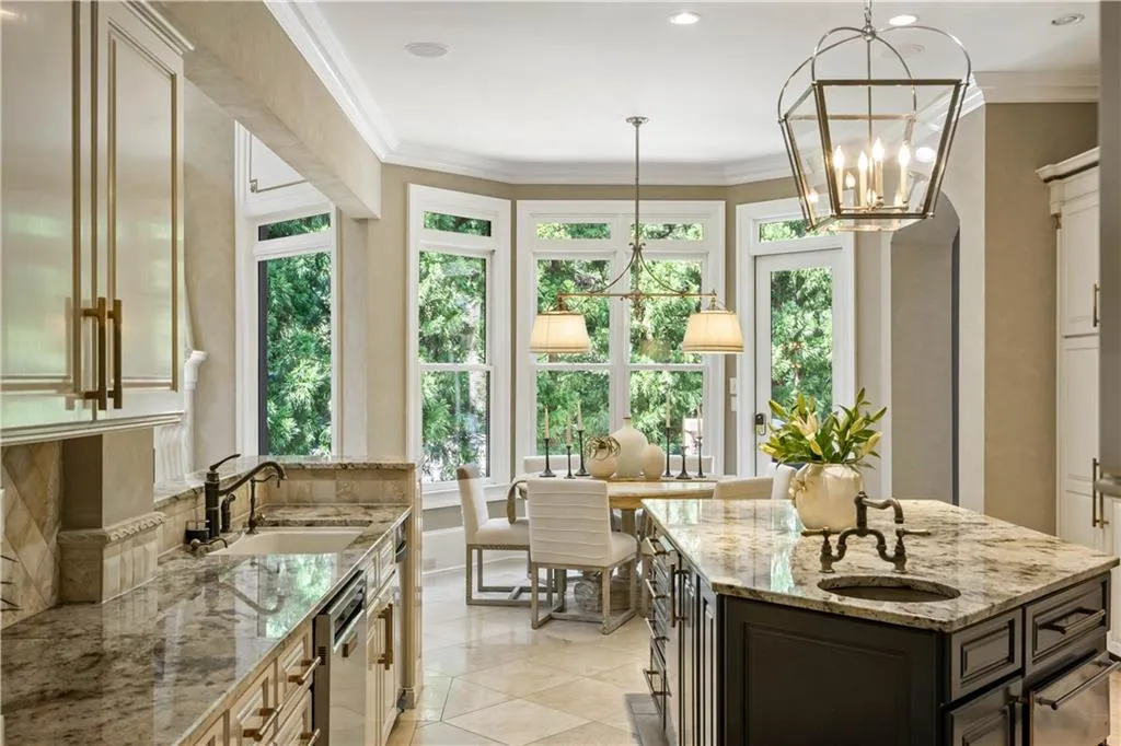 Kitchen featuring decorative light fixtures, a notable chandelier, a kitchen island with sink, sink, and light stone counters