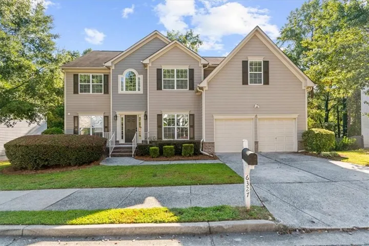 Two-story residence featuring a dual-tone facade, arched window detailing, a two-car garage, established front landscaping, and a paved driveway