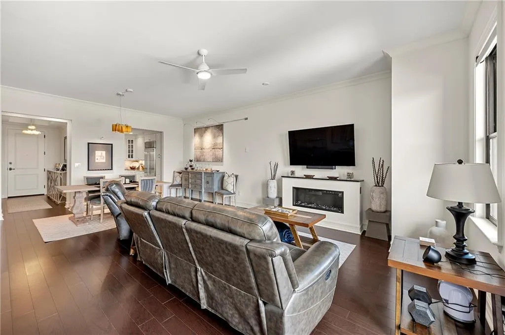 Living room featuring a glass covered fireplace, ornamental molding, dark wood floors, and ceiling fan