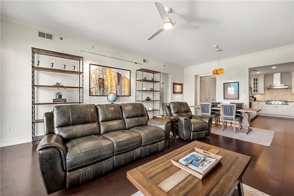 Living area featuring baseboards, visible vents, ceiling fan, wood flooring, and crown molding