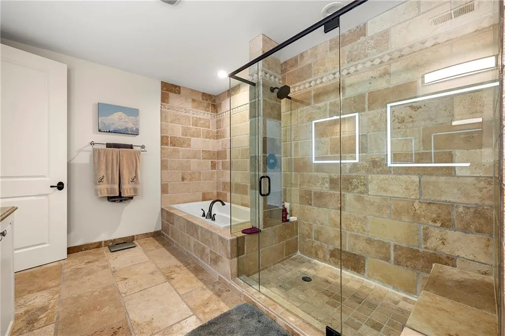 Primary Bathroom featuring stone tile floors, a stall shower, baseboards, and a garden tub