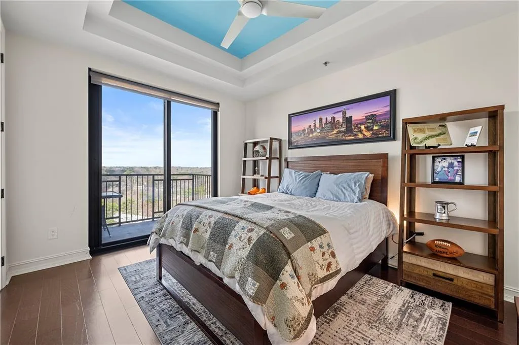 Bedroom with hardwood / wood floors, baseboards, a tray ceiling, ceiling fan, and access to outside