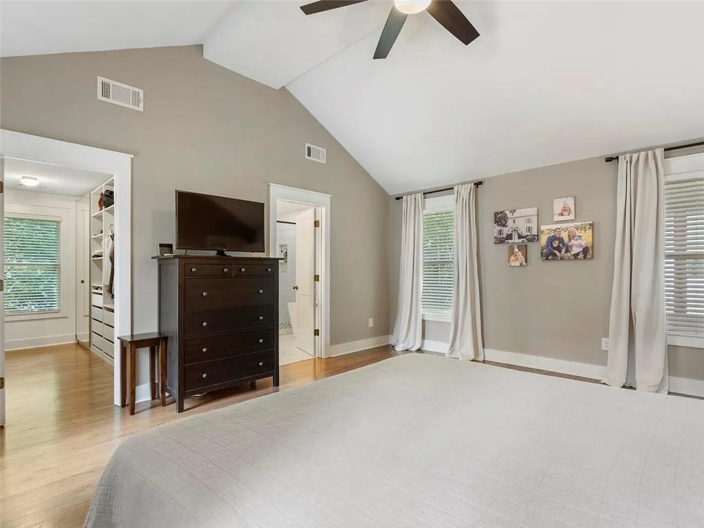 Bedroom featuring ensuite bath, hardwood / wood-style flooring, ceiling fan, and multiple windows