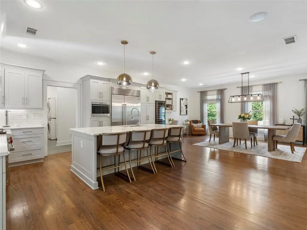 Kitchen featuring stainless steel appliances, a kitchen bar, an island with sink, wood-type flooring, and pendant lighting