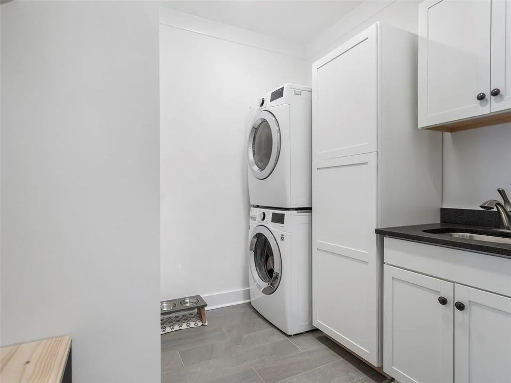 Clothes washing area featuring stacked washer / dryer, cabinets, and sink