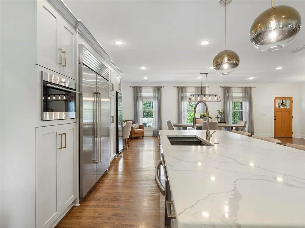 Kitchen featuring an island with sink, stainless steel appliances, light stone counters, and hardwood / wood-style flooring