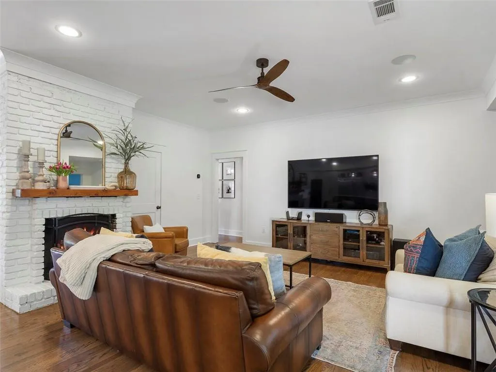 Living room featuring hardwood / wood-style floors, ceiling fan, a fireplace, and crown molding