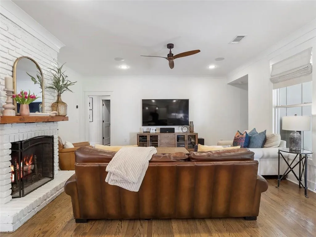 Living room with crown molding, hardwood / wood-style flooring, a brick fireplace, and ceiling fan
