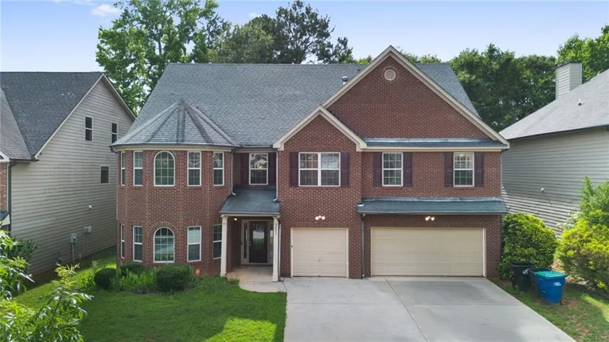 Brick-front two-story residence featuring a prominent turret with arched windows, two separate garage doors, and dark window shutters
