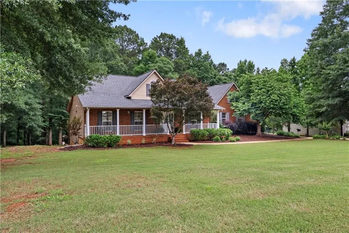 Brick facade home with a covered front porch, white railing, mature landscaping, and a pitched roofline