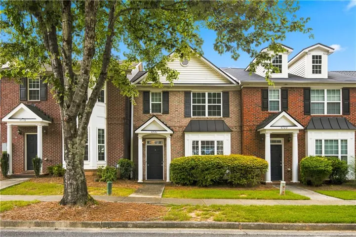 Brick townhouse exterior featuring white siding gables, black window shutters, and a covered entry porch with white columns