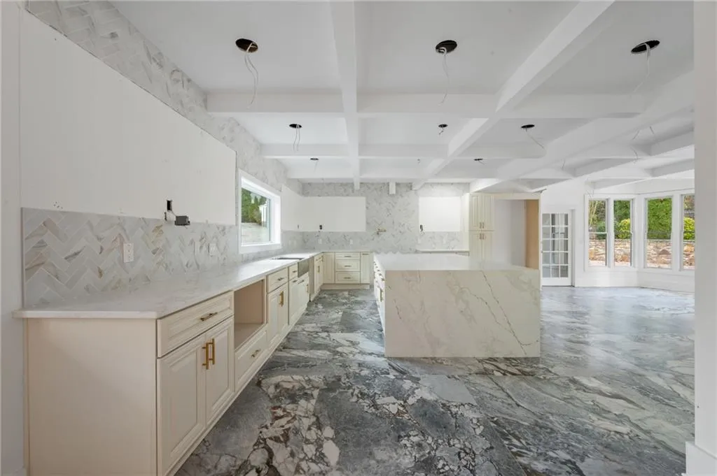 Kitchen with coffered ceiling, cream cabinets, decorative backsplash, light stone countertops, and beam ceiling