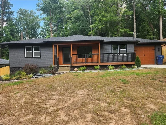 Contemporary ranch-style exterior with dark gray brick, a wood-finish garage door, and a covered front porch featuring dark wood pillars and railings