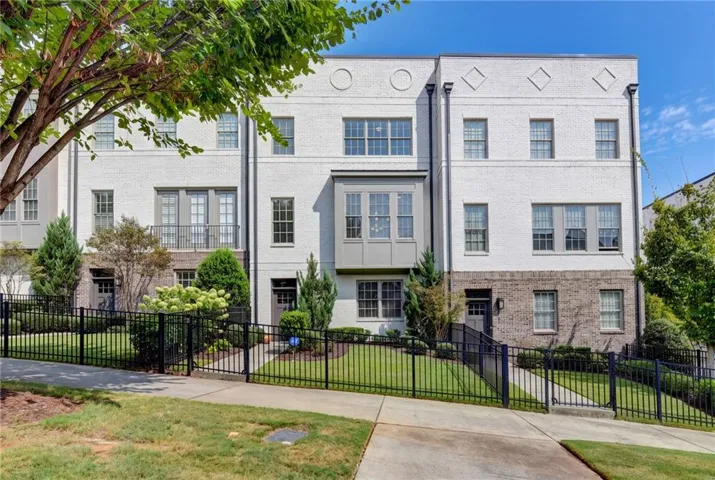White brick exterior with gray trim windows, bay window feature, and black wrought iron fencing
