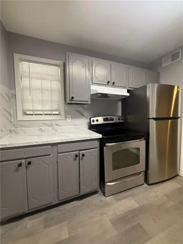 Kitchen featuring stainless steel electric range, light countertops, gray cabinets, and light wood-style flooring