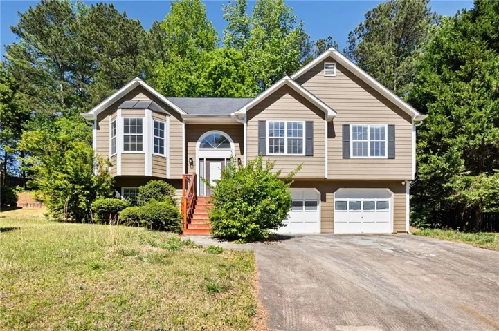 Elevated split-level home featuring tan vinyl siding, multiple gabled rooflines, and a welcoming front entrance with red brick steps