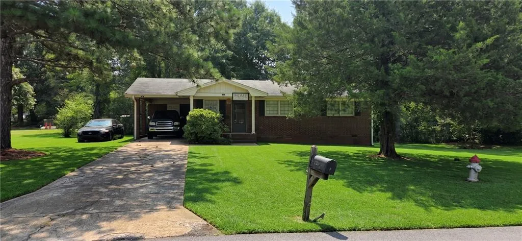 Brick façade ranch-style home with an attached carport, covered front porch, and mature trees