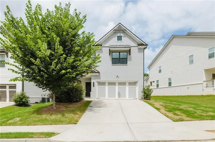 Modern two-story residence featuring a clean white exterior with gable roofline, two-car garage with paneled doors, and a wide concrete driveway