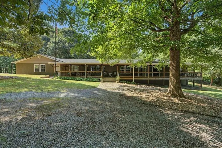 Ranch-style exterior with a covered front porch, gravel driveway, and mature trees