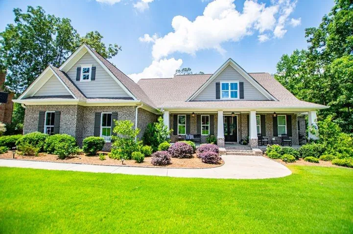 Exterior featuring brick and horizontal siding, a covered front porch with white columns, a gabled roofline, dark shutters, and a concrete pathway