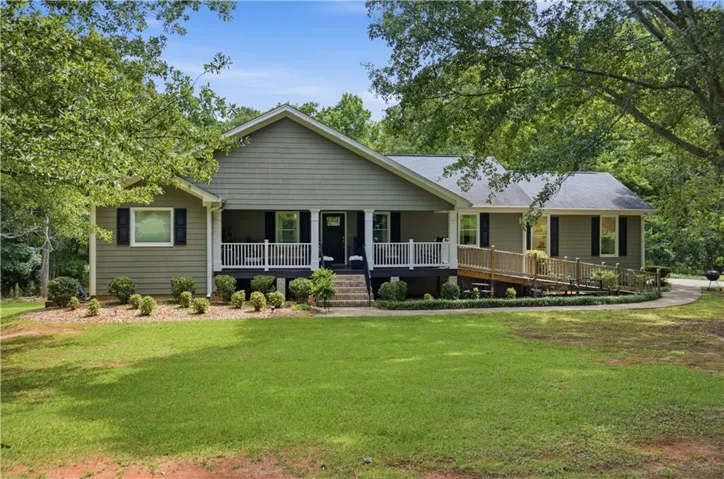 Ranch-style exterior with siding, a covered front porch with white railing, a wood ramp entry, and mature landscaping